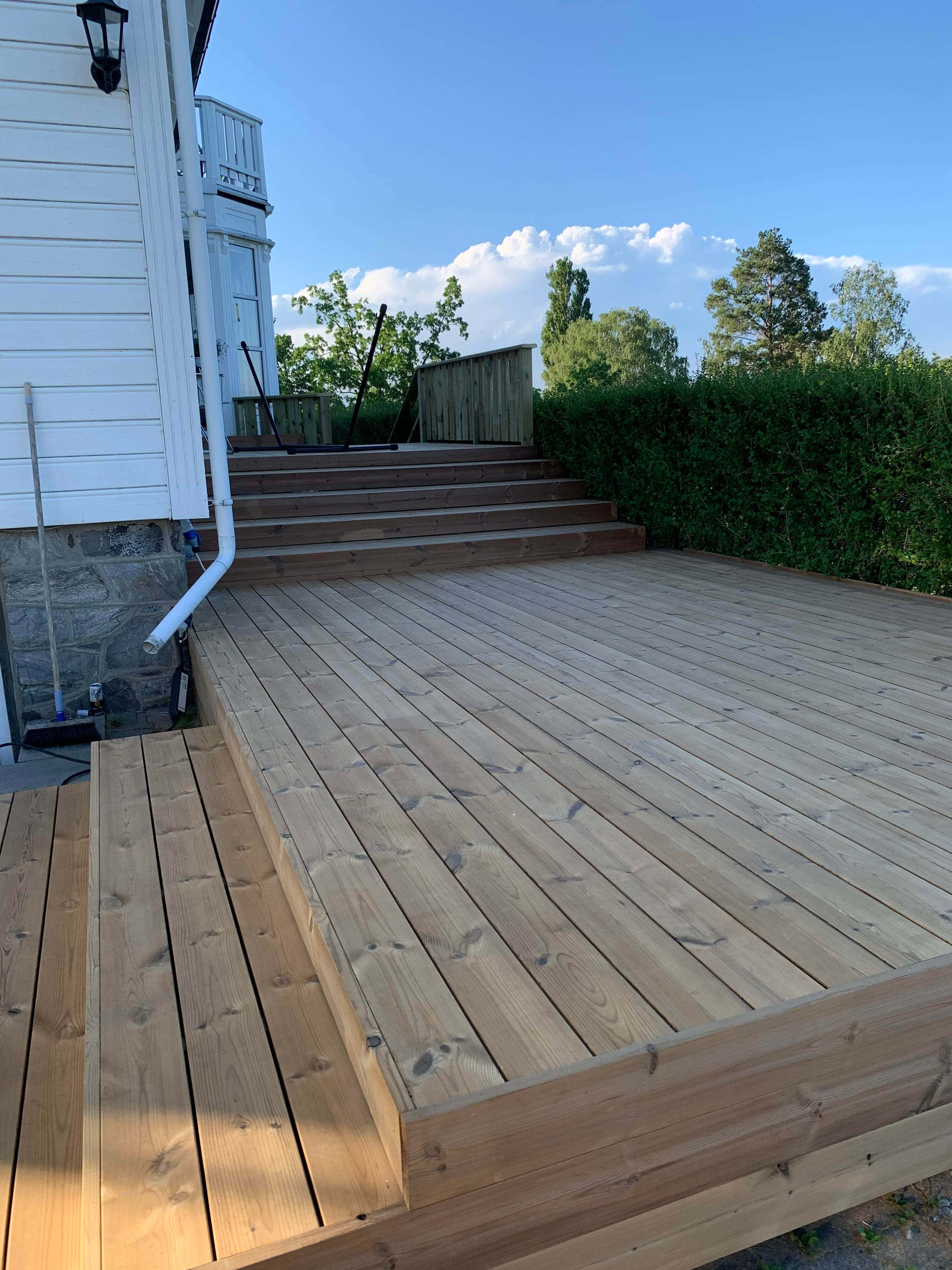 Freshly finished multi-level wooden deck with wide stairs, next to white house