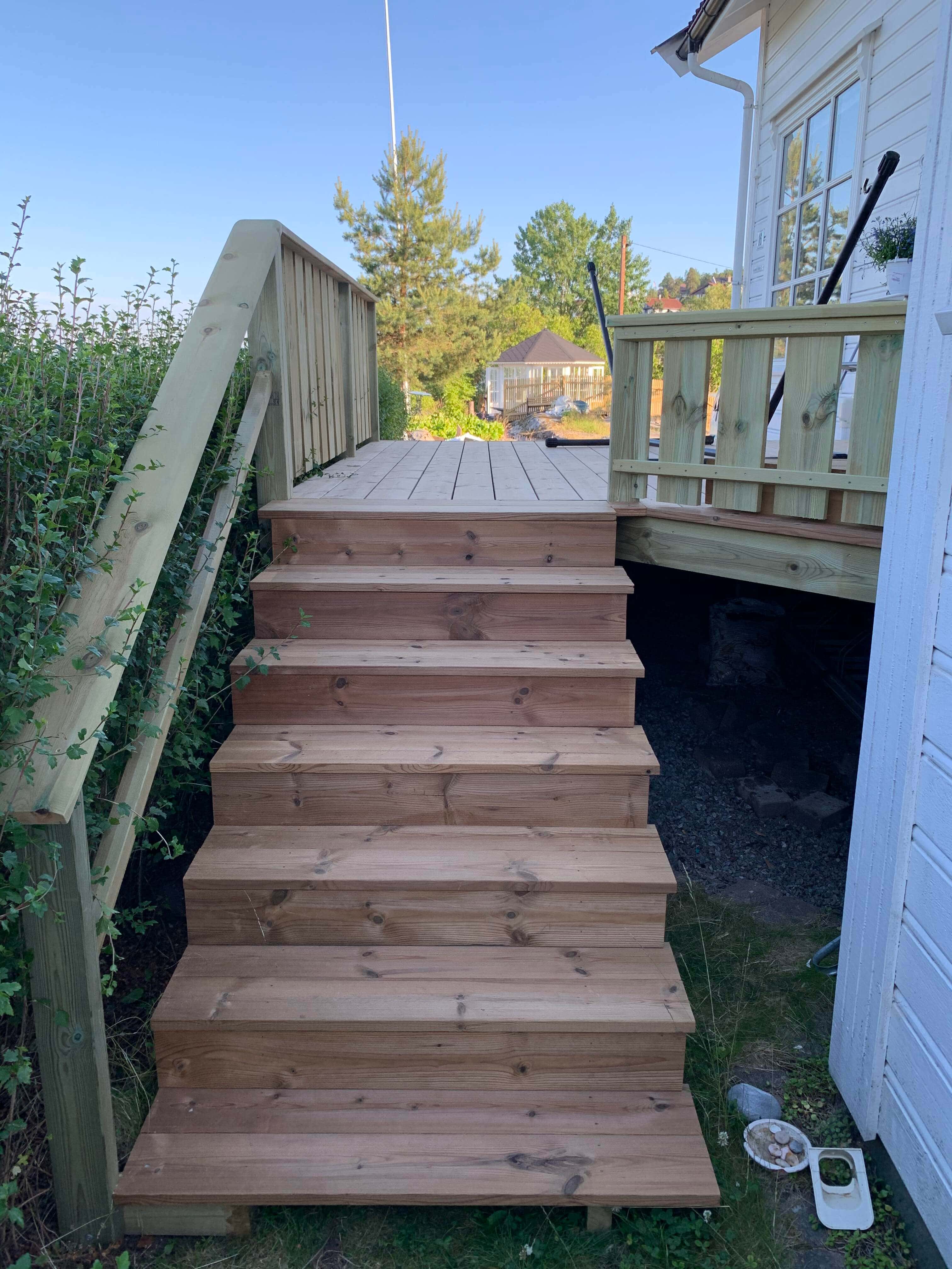 Sturdy wooden stairs leading to elevated deck with railings and garden view