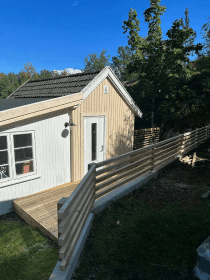 New wooden terrace with horizontal slat fence beside small house